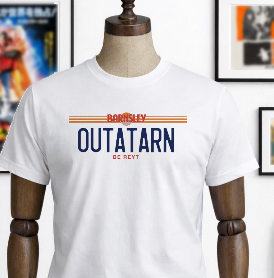 White t-shirt with 'Outatarn' text on a mannequin, with a colorful skateboard and framed posters in the background.